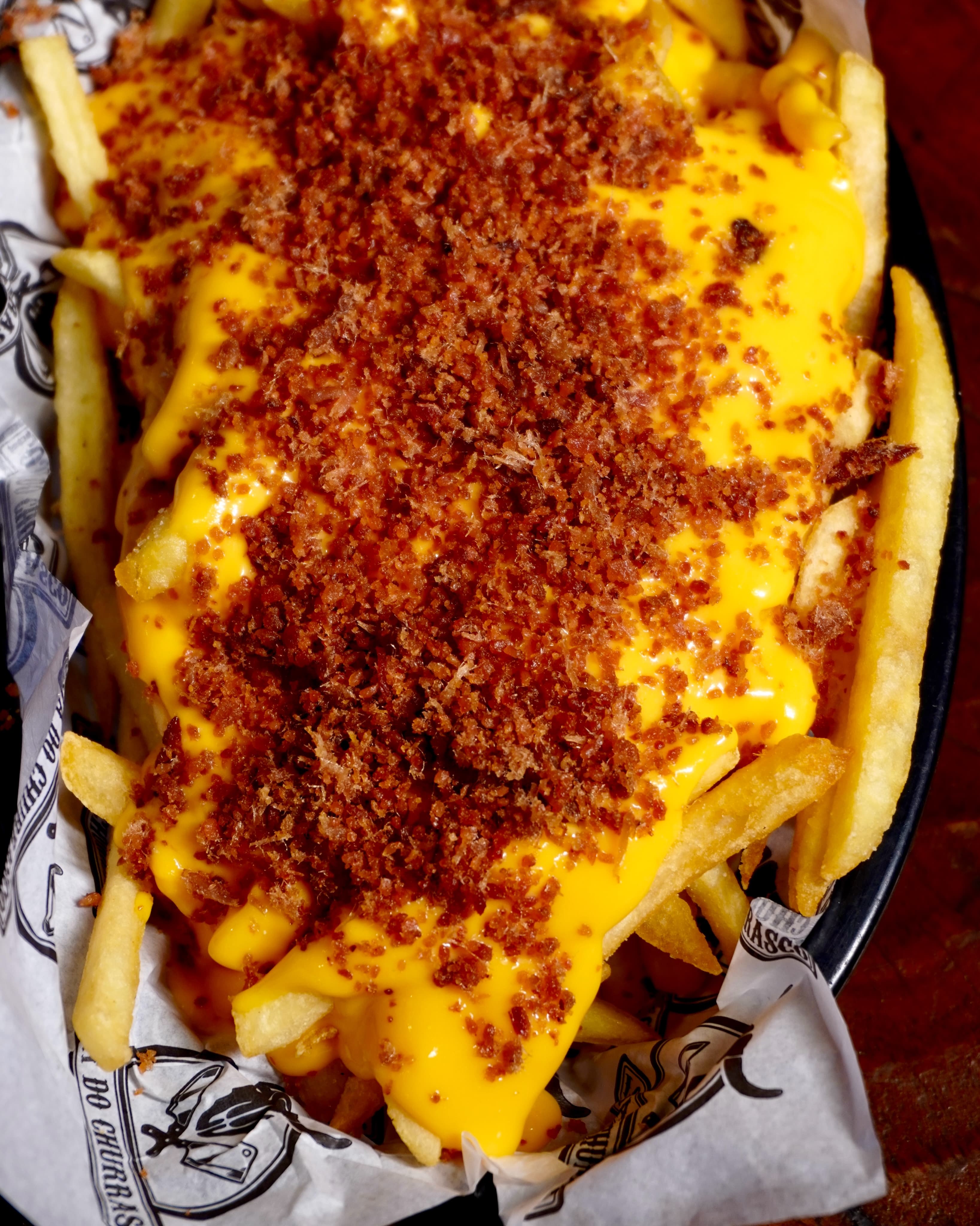 Batata frita com cheddar e farofa de bacon no papel da casa