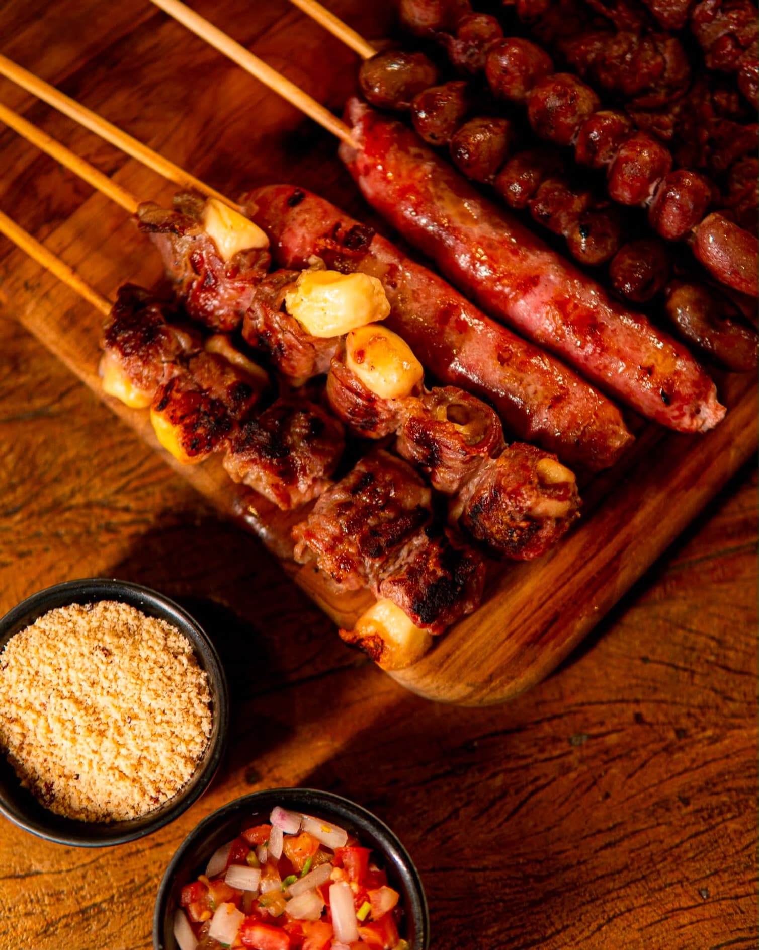 Tábua com espetinhos de carne com queijo, linguiça e coração, farofa e vinagrete